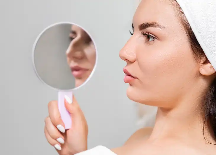 Woman looking at her Rhinoplasty Recovery in the mirror